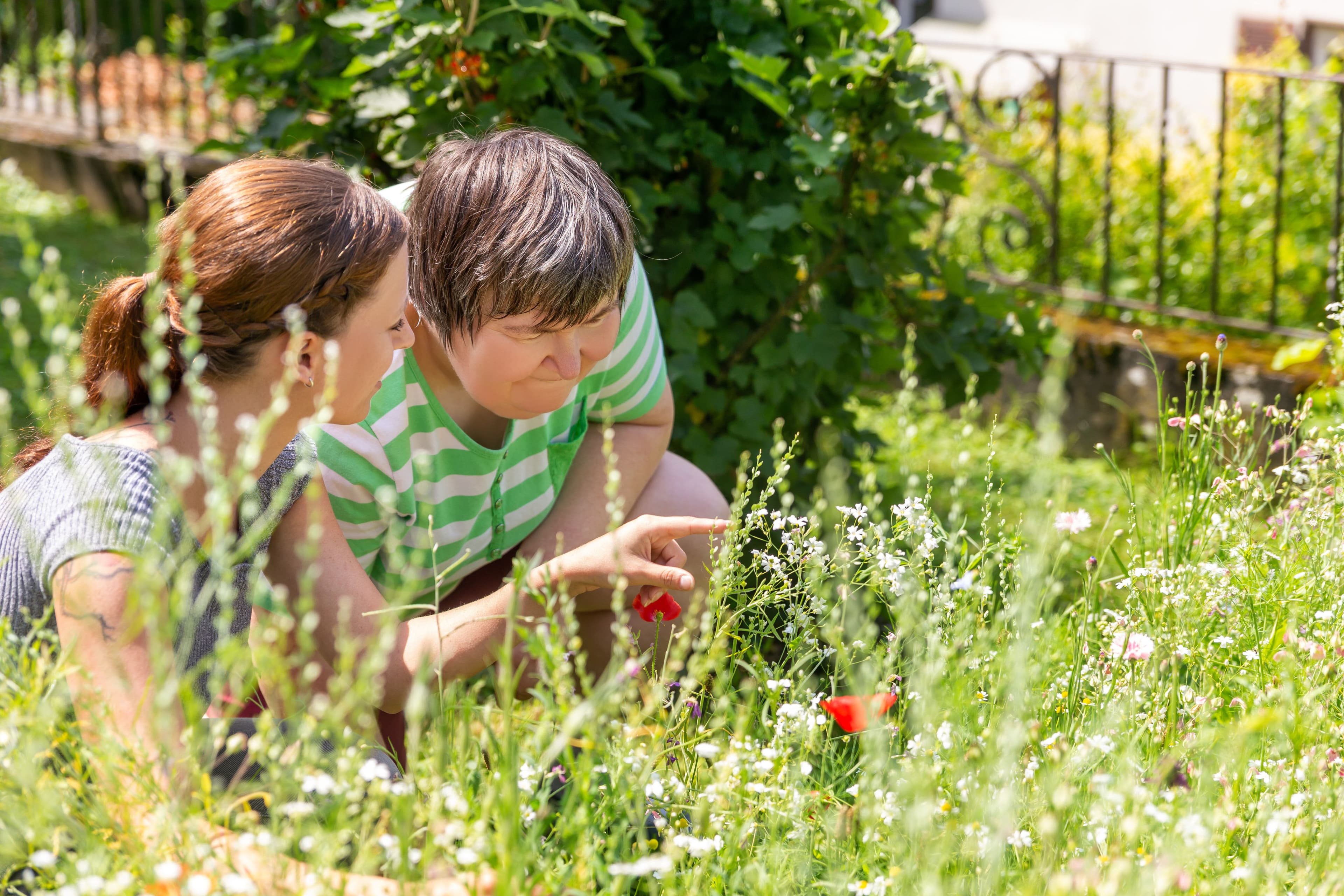 A woman and a person with disability are crouched down in a garden.